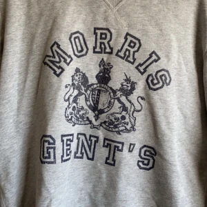 Grå sweatshirt från Morris - Säljer en snygg grå sweatshirt från Morris med tryck framtill. Tröjan har långa ärmar och en klassisk rund halsringning. Perfekt för en avslappnad stil eller att bära till vardags. Passar bra till jeans eller chinos!