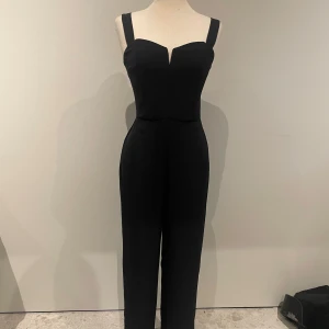 Byxdress - Snygg svart byxdress med breda axelband och en figurnära passform. Den har en dragkedja i ryggen för enkel påklädning. Passar bra till både fest och annat