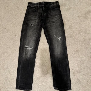 Svarta jeans från Jack & Jones - Säljer ett par svarta jeans från Jack & Jones i bra skick. De har en cool slitningseffekt och är i tapered fit, vilket ger en snygg och modern look. Perfekta för både vardag och fest! 