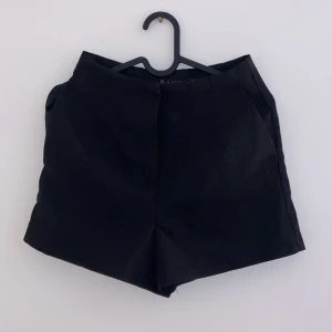Svarta shorts - Säljer ett par stilrena svarta shorts i mycket bra skick. De har en klassisk design med dragkedja och knappar framtill. Perfekta för både vardag och fest! Passar till alla tillfällen och är ett måste i garderoben.