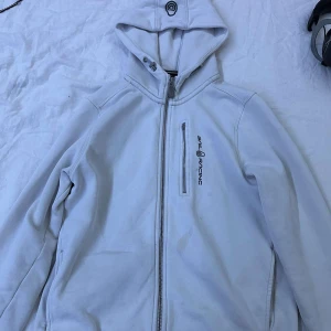 Vit hoodie från Sail Racing - Säljer en vit hoodie från Sail Racing  Den har en dragkedja framtill och en luva. Den har dock en liten fläck där fram men den går säkert bort om man har bra medel till de. Hör av dig vid intresse!