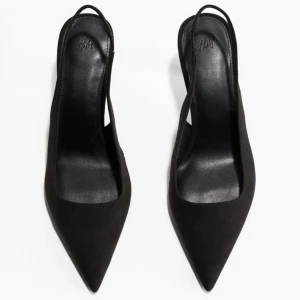 Svarta pumps från H&M - Snygga svarta pumps från H&M med spetsig tå och elegant klack. Perfekta för både fest och mer formella tillfällen. De har en stilren design med en smal rem runt hälen för extra komfort.