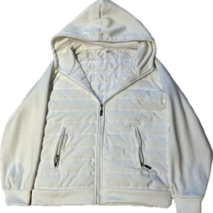 Vit quiltad hoodie - Säljer en superskön och stilren vit cardigan med quiltad framsida. Den har en dragkedja och två praktiska fickor med dragkedjor. Perfekt för kyliga dagar och passar till nästan allt. Den är i nyskick! Även en extremt eftertraktad jacka!