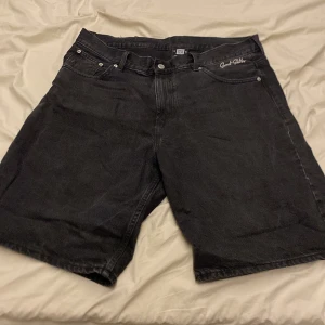 Svarta jeansshorts från Sweet SkTbs - Säljer ett par svarta jeansshorts från Sweet SkTbs i storlek L. De har en klassisk femficksdesign med knapp och dragkedja framtill. Perfekta för en avslappnad stil under sommaren. Shortsens material är slitstarkt och bekvämt, vilket gör dem idealiska för vardagsbruk.