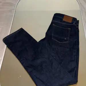 Säljer ett par mörkblå Tommy Hilfiger jeans i straight fit. De är i bra skick och har en klassisk design med fem fickor och knappgylf. Perfekta för både vardag och fest!