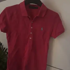 Säljer en snygg rosa pikétröja från Ralph Lauren. Den har en klassisk krage och knappar framtill. Perfekt för en avslappnad men stilren look. Den ikoniska loggan är broderad i blått på bröstet. Passar perfekt till både vardag och fest!