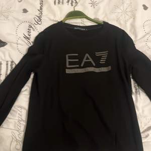 Säljer en stilren svart tröja från Emporio Armani med EA7-logga på framsidan. Tröjan är långärmad och perfekt för både vardag och fest. Den är i mycket bra skick och passar perfekt till höst- och vintergarderoben. Skön och enkel att matcha med andra plagg!