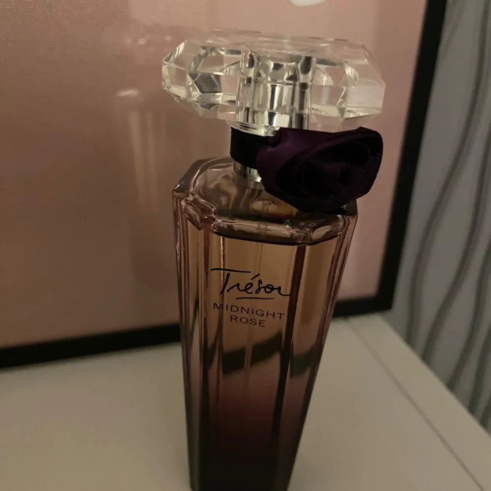Säljer en elegant Trésor Midnight Rose parfym från Lancôme. Flaskan är lila och har en vacker kristalliknande kork. Den har en mörk och mystisk doft, perfekt för kvällar. En liten rosett pryder flaskhalsen för en extra touch av lyx.. Perfume.