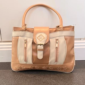 Beige handväska  - Beige handväska i fint skick med många detaljer. 33 cm bred, ca 23 cm hög och 8 cm djup. Vet inte vad det är för märke. Kom privat för fler bilder. Använd gärna köp nu!