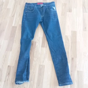 Blå jeans från Replay - Säljer ett par snygga blå jeans från Replay i storlek 30. De är i bra skick och har en klassisk femficksdesign med en knapp och dragkedja framtill. Jeansen har en normal passform och är perfekta för vardagsbruk. De har också snygga detaljer på bakfickorna.