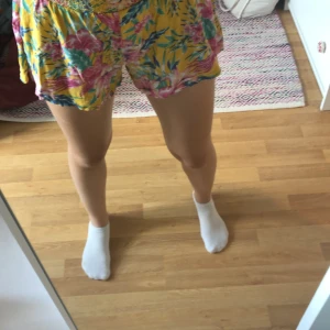 Färgglada blommiga shorts - Säljer ett par superhärliga shorts med blommigt mönster i olika färger. De är gula i grunden med blommor i rosa, blått och grönt. Perfekta för sommaren! De är lösa och bekväma, idealiska för varma dagar. Passar perfekt till stranden eller en avslappnad dag ute. Passar mig som har S/164-170