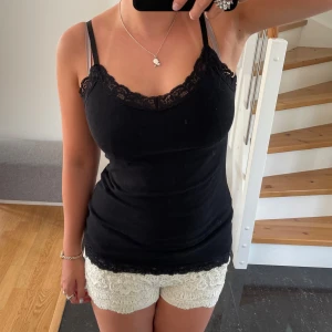 Svart linne med spetsdetaljer - Säljer ett svart linne med spetsdetaljer runt halsringningen. Linnet har smala axelband och är perfekt för sommaren. Det är i bra skick och passar till både vardag och fest. Perfekt att matcha med shorts eller kjol! Vet inte vart den är ifrån eller storlek men skulle säga M, den är ifrån min mammas garderob så det är inte Shein!