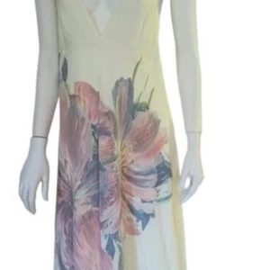 Vit långklänning med blommigt mönster - Säljer en superfin vit långklänning med ett stort blommigt mönster i rosa, lila och grönt. Klänningen har en djup v-ringning och är ärmlös, vilket gör den perfekt för sommarens alla fester. Den har också en öppen rygg som ger en extra touch av elegans. Materialet känns lätt och luftigt, perfekt för varma dagar. Passar perfekt till tex ett bröllop? Eller annan fest?