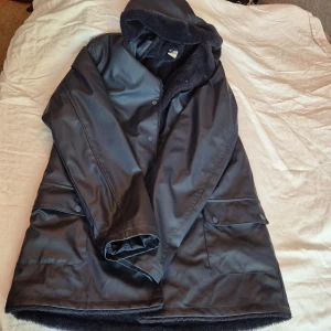 Svart jacka från Lindex - Säljer en svartblå regnjacka från Lindex i storlek 170. Jackan har en huva och är fodrad med mjukt material på insidan. Den har långa ärmar och stängs med knappar. Perfekt för kalla dagar!