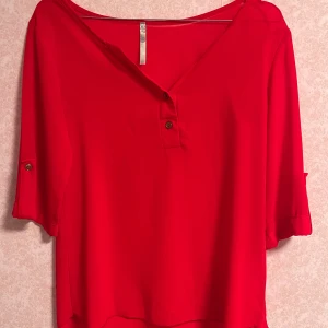 Röd blus med knappar - Säljer en snygg röd blus med knappar framtill. Blusen har trekvartsärmar med knappdetaljer och en lös passform.