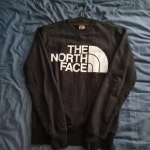 Säljer en svart sweatshirt från The North Face i storlek S. Tröjan är i ny skick och har en stor logga på framsidan samt en mindre logga på bröstet. Perfekt för höst och vinter, den är både snygg och bekväm. Passar till både vardag och träning.