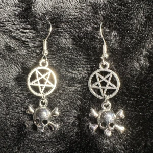 Unika nya örhängen med pentagram och dödskallar Nya Ockult Satanic Unika Metal Rock Punk Biker Bundlerabatt  - Säljer ett par riktigt coola silverfärgade örhängen med pentagram och dödskallar med korslagda benknotor.  Längd ca 5,6 cm, bredd 0,8 cm.   Hypoallergena krokar.   Gummistoppar medföljer.  Nytillverkat och egendesignat av mig @bybasen.   Ett unikt smycke och en uppseendeväckande present till dig själv eller någon du tycker om.  Jag skickar sålda varor en eller två gånger i veckan. Säg till om du har bråttom så ordnar jag det snabbare.  Jag prutar inte men ger bundlerabatt.