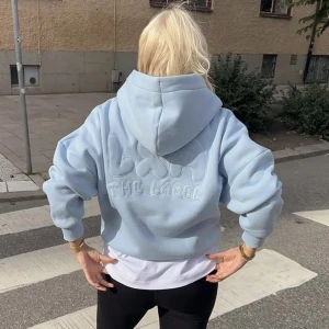 Ljusblå hoodie från LXA The Label - Supermysig ljusblå hoodie från LXA The Label. Perfekt för chill dagar eller när du vill ha en avslappnad stil. Den har en stor luva och ett snyggt broderat märke på ryggen. Passar perfekt över en t-shirt eller linne.