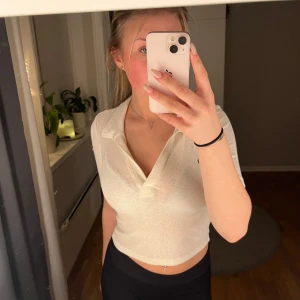 Vit ribbad polotopp - Säljer en snygg vit ribbad polotopp med korta ärmar. Toppen har en tight passform och är perfekt för både vardag och fest. Den är i mycket bra skick.