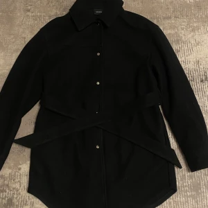 Svart kappa från Vero Moda - Säljer en stilren svart kappa från Vero Moda i storlek S. Den har långa ärmar och knappar framtill. Perfekt för höst och vår, och den har ett bälte i midjan för en snygg passform. Passar både till vardags och festliga tillfällen. Har endast använt ett par gånger vid fina firanden. Finns ej att köpa från hemsidan längre. Ingen slitage alls! Priset kan diskuteras. 