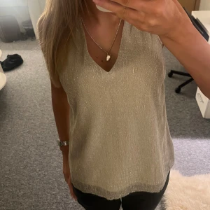 Guldglittrig topp/blus💘 - Säljer en snygg glittrig topp i guld med v-ringning. Perfekt för festliga tillfällen! Toppen är ärmlös och har en lös passform som gör den bekväm att bära samtidigt som den är sjukt snygg🧡🧡
