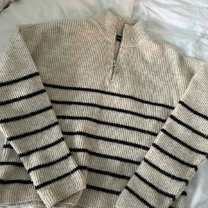 Beige och svart randig stickad tröja - Mysig beige stickad tröja med svarta ränder och dragkedja vid halsen. 