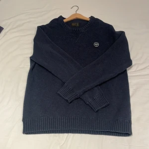 Morris crewneck - Säljer en snygg mörkblå stickad tröja från Morris. Den har en rund halsringning och ett stilrent märke på bröstet. Perfekt för kyliga dagar och passar både till vardags och lite finare tillfällen. Tröjan har långa ärmar och ribbade kanter för en skön passform. Köpt på rea för 1500 men jag säljer den för 699 men kan gå ner i pris vid snabb affär!