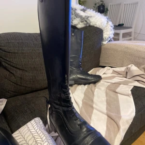 Svarta ridstövlar - Säljer ett par svarta ridstövlar i skinn med snörning framtill. De är i bra skick och perfekta för ridning. Stövlarna har en robust sula och är designade för att ge bra stöd och komfort under ridturer.