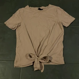 Beige/rosa kortärmad topp från Object - Säljer en superfin beige/rosa kortärmad topp från Object i storlek XS. Den har en snygg knytdetalj framtill som ger en cool look. Perfekt för både vardag och fest! 🥰