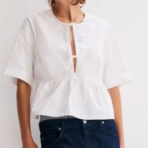 Vit blus med knytning - Säljer en superfin vit blus från Monki i bomull. Den har korta ärmar och en söt knytning framtill. Perfekt för alla tillfällen! Blusen har en luftig passform och en volangdetalj vid midjan. Passar både till jeans och kjol för en avslappnad look. 
