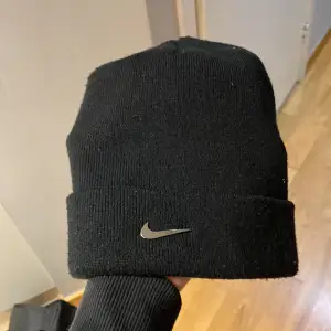 Säljer en svart stickad mössa från Nike i mycket bra skick. Den har en snygg, enkel design med en liten metall-logga framtill. Perfekt för höst och vinter för att hålla dig varm och stilren. Passar de flesta tack vare sin flexibla passform💯orginal pris 350kr