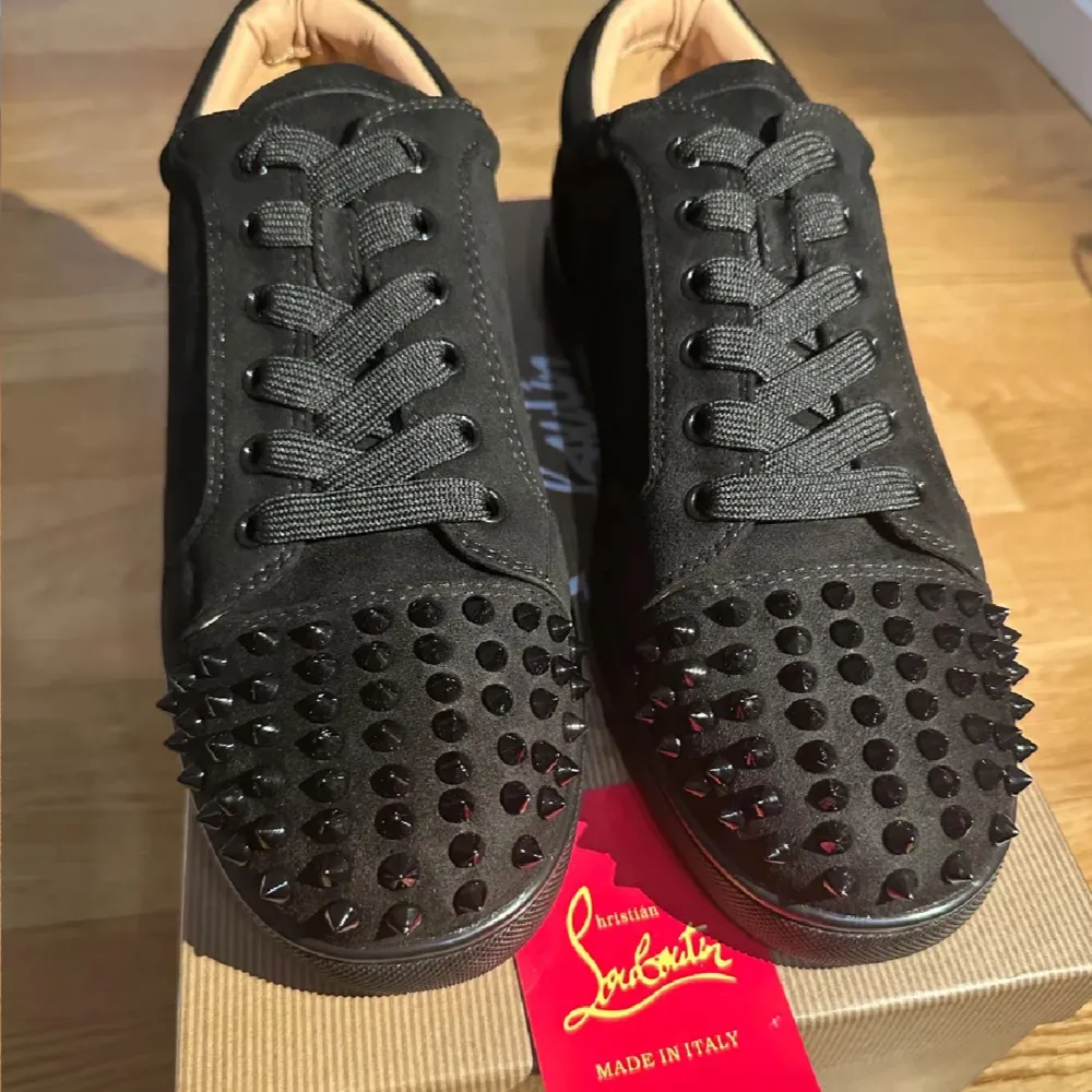 Säljer ett par svarta sneakers från Christian Louboutin i storlek 43. Skorna har en cool design med nitar på tån och en ikonisk röd sula. De är i mycket bra skick och perfekta för att ge din outfit en edgy touch. Passar både till vardags och fest!. Skor.