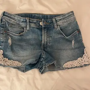 Säljer ett par snygga blå jeansshorts från H&M i storlek 152. De har coola slitningar och fina vita spetsdetaljer vid benen. Perfekta för sommaren och ger en avslappnad men stilren look. Passar både till stranden och en dag på stan! Dom är ganska korta men är ändå super snygga på!