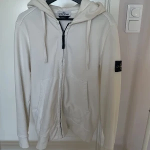 Stone island hoodie - Säljer en snygg vit hoodie från Stone Island i mycket bra skick. Den har en dragkedja framtill och en klassisk huva med dragsko. På ärmen finns det ikoniska Stone Island-märket. Perfekt för både höst och vår! Hör av dig om du funderar över något mvh Leo 😊