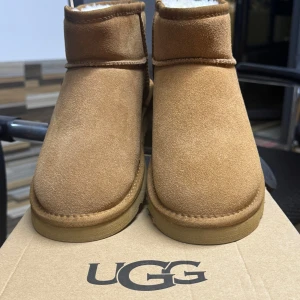 Bruna UGG boots i mocka - Säljer ett par klassiska bruna UGG boots i mjuk mocka. De har en fluffig insida som håller fötterna varma och sköna under kalla dagar. Perfekta för höst och vinter! De är i nytt skick och kommer i originalkartong.