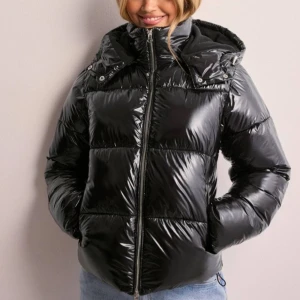  Shiny puffer jacket - Säljer en supercool svart pufferjacka med glansigt material och huva. Perfekt för vintern med sin varma och mysiga stil. Köpte den för ungefär 1 månad sen.