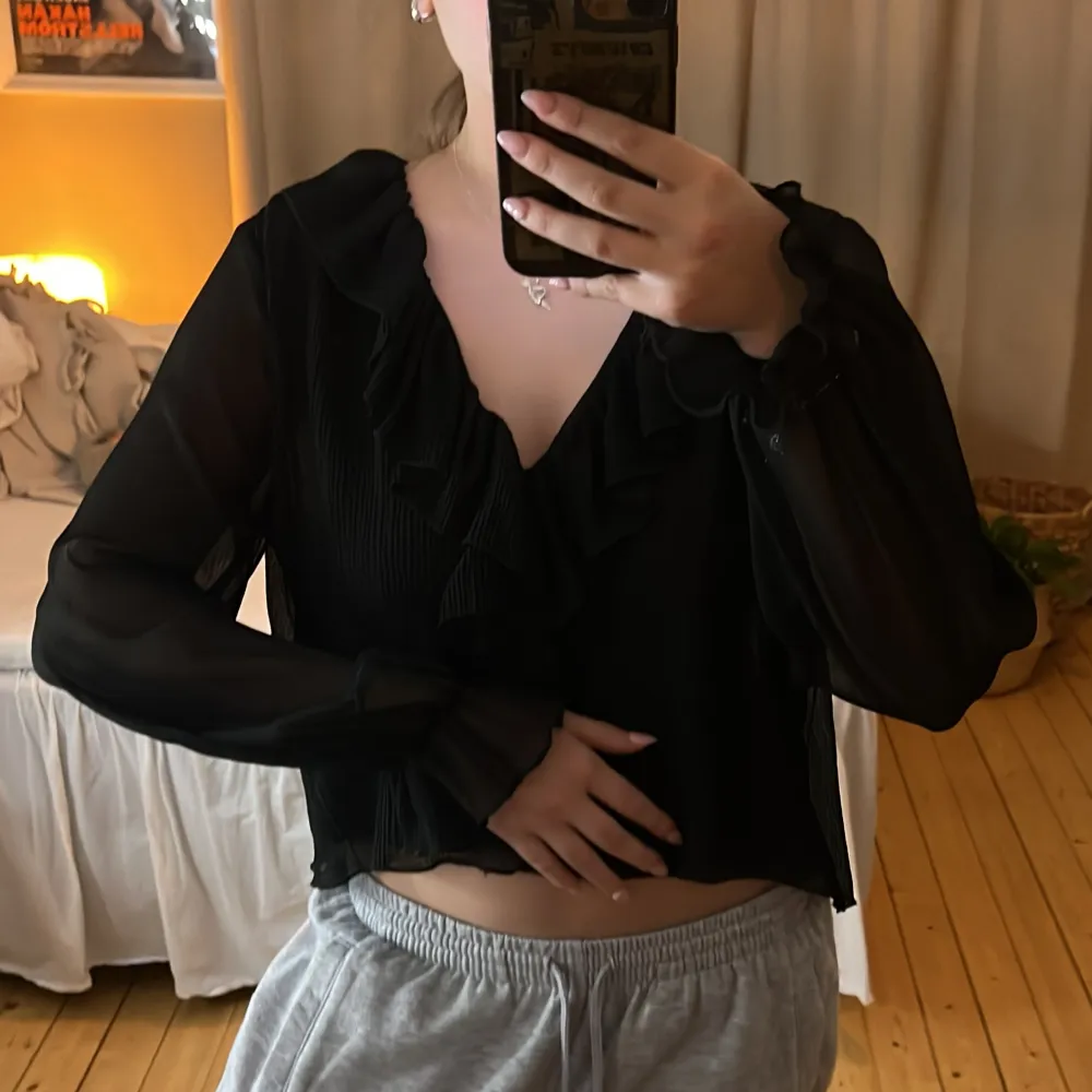Snygg svart blus med volangdetaljer och långa ärmar. Perfekt för en stilren look. Blusen har en lätt transparent design och en v-ringad halslinje. Storlek xs!. Yläosat.