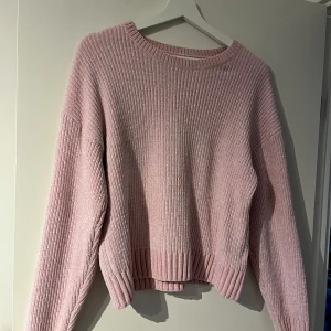 Rosa stickad tröja - Mysig rosa stickad tröja med ribbad struktur. Tröjan har långa ärmar och en avslappnad passform, perfekt för kyliga dagar.