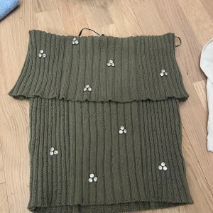 Olivgrön offshoulder topp från Zara - Snygg olivgrön offshoulder topp från Zara med ribbad struktur och dekorativa pärlor. Perfekt för att ge en stilren touch till din outfit. Toppen har en elegant volangdetalj vid axlarna.