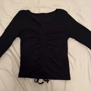 Svart ribbad topp med knyt - Snygg svart ribbad topp med långa ärmar och knytning framtill. Den är i storlek xs men passar även s.