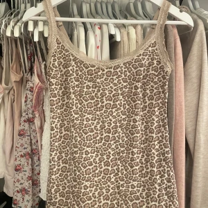 Leopardmönstrad pyjamaslinne från Trofé - Säljer ett snyggt leopardmönstrat pyjamaslinne från Trofé i storlek S. Linnet har spetsdetaljer vid halsringningen och axelbanden samt en liten rosett framtill. Materialet är mjukt och stretchigt, perfekt för en trendig look. Banden är justerbara. ❄️🌸 öppen för prisförslag!!