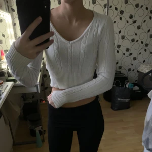 Vit croppad stickad tröja - En vit croppad kabelstickad tröja. Tröjan har en v-ringad design och långa ärmar med ribbade muddar. Använd ett fåtal gånger.