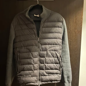 Grå quiltad jacka från Moncler - Snygg grå quiltad jacka från Moncler med dragkedja och långa ärmar. Jackan har en stilren design med Moncler-logga på ärmen och ribbade detaljer vid kragen. Perfekt för kyligare dagar.