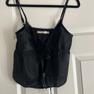 Svart linne från NA-KD - Snygg svart linne från NA-KD med smala axelband och knytning framtill. toppen har spetsdetaljer!! 