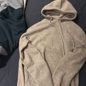 Beige stickad hoodie - Mysig beige stickad hoodie med långa ärmar och ribbade muddar. Perfekt för kyliga dagar med sin bekväma passform och klassiska design.