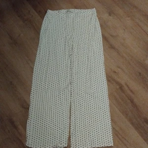 Vita byxor med hjärtmönster - Charmiga vita byxor med röda hjärtan. De har en loose passform och är högmidjade, vilket ger en bekväm och stilren look. Perfekta för en avslappnad dag.