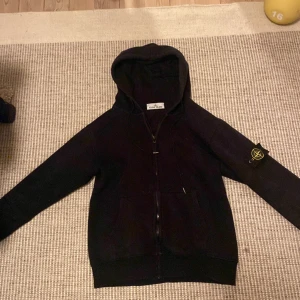 Svart hoodie från Stone Island - Säljer en svart hoodie från Stone Island med dragkedja och huva. Den har en broderad logotyp på ärmen.  Pris kan diskuteras vid snabb affär 