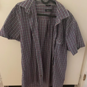 Rutig kortärmad skjorta - Snygg rutig skjorta i blått, rött och vitt. Skjortan har korta ärmar och knappar framtill. Perfekt för en avslappnad stil.
