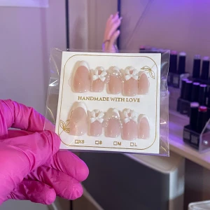 Handgjorda naglar med rosetter och pärlor  - Säljer ett set med handgjorda naglar i en mjuk rosa nyans, dekorerade med vita rosetter. Perfekt för en elegant och unik look. 