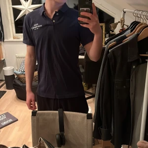 Mörkblå pikétröja från Peak Performance - Säljer en stilren mörkblå pikétröja från Peak Performance. Tröjan har korta ärmar och en klassisk krage med knappar. Perfekt för en avslappnad men ändå snygg look.